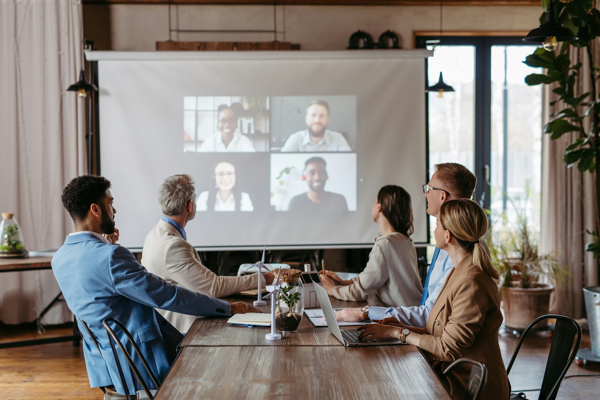 Employees having online business conference video call on screen monitor in board meeting room.