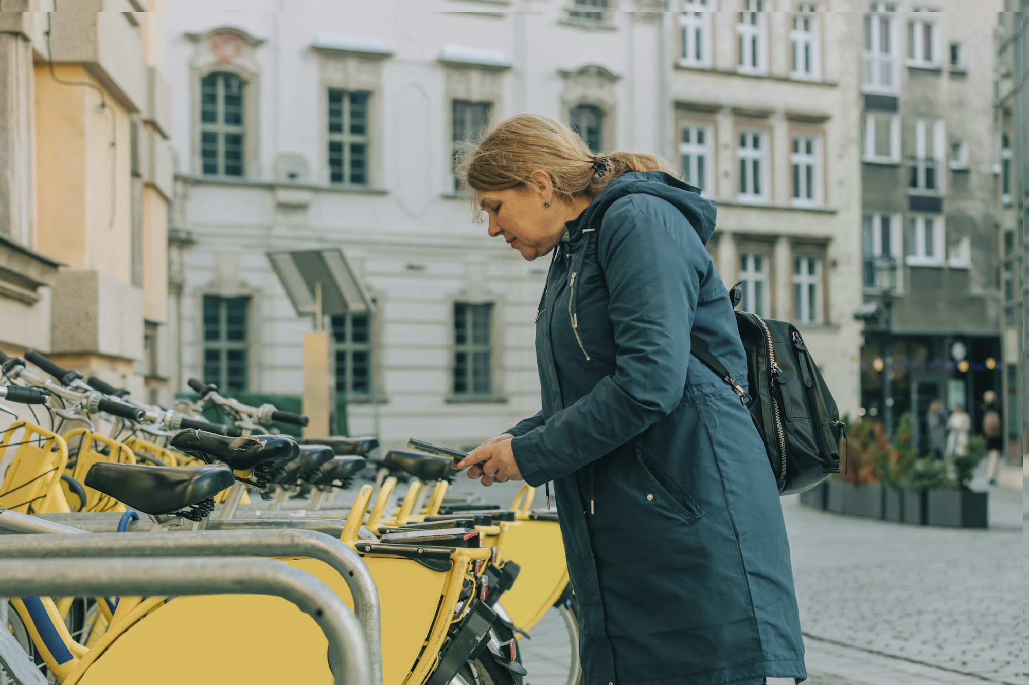 Senior woman try to rent a bike by using app on mobile phone, Wroclaw, Poland